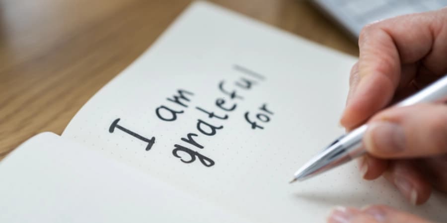 7 Reasons to Start Journaling During Your AA Journey Someone writing on an open journal with the phrase "I am grateful for", showing their gratitude after attending AA meetings