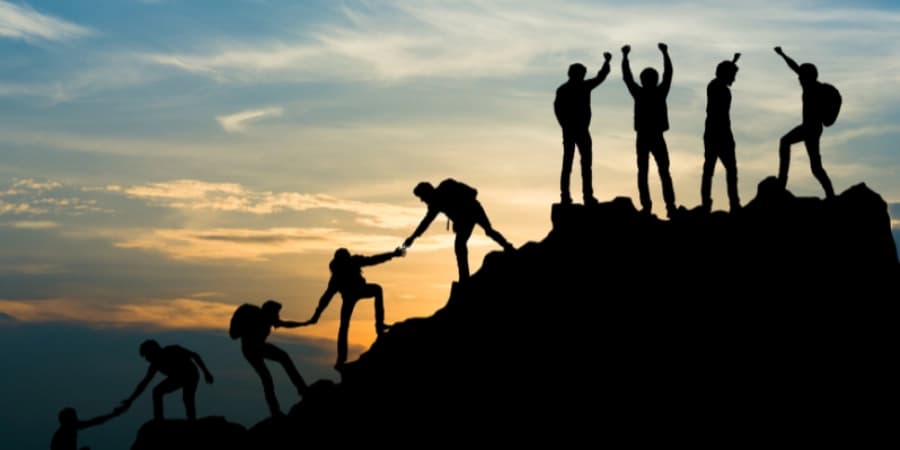 The Truth About AA Meetings A group of people helping each other up a mountain, symbolizing the AA community helping one another